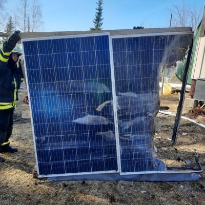 Pelastuslaitoksen työntekijä pitelee palanutta aurinkopaneelia.