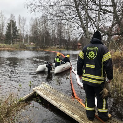 Pelastaja rannalla ja kaksi veneessä asettelemassa öljypuomia.