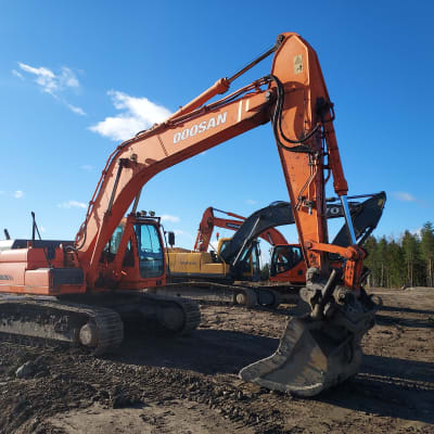 Flera orange och gula grävmaskiner på byggplats.