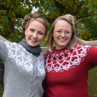 Två kvinnor leende utomhus med en stor sjal om axlarna.