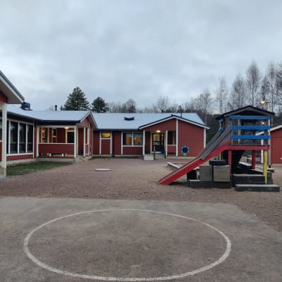 Ett rött hus som är ett daghem, Kila daghem i Karis. På gården syns en klättertsällning med rutschkana.