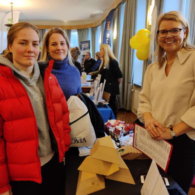 Tre kvinnor står vid ett bord där en yrkeshögskolautbildare visar sitt utbud. De heter Emilia Bäckström, Annika Lindholm och Bella Alén.