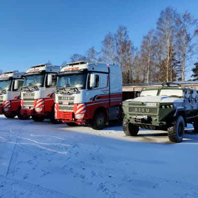 Ett militärfordon och tre dragbilar till lastbilar står bredvid varandra på en gårdsplan.