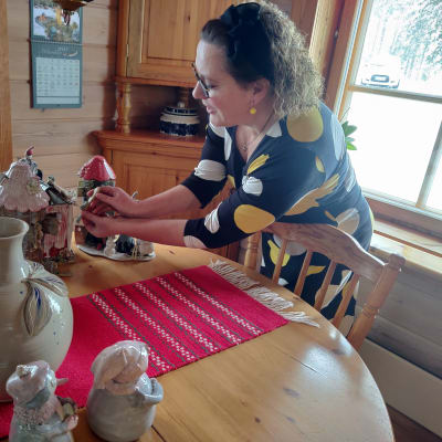 En kvinna står vid ett bord och fixar med tre små hus i keramik. Hon heter Nina Barrett.