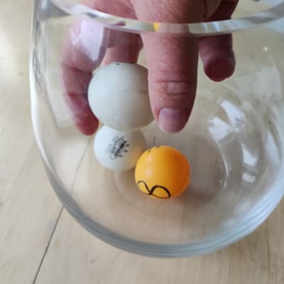 Tre pingisbollar i en glasburk, en hand lyfter upp en av bollarna.