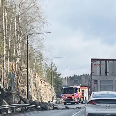 En hög stora stenar har rasat in på en bilväg. I bakgrunden syns en brandbil.