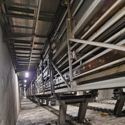 En lång betongtrappa går ner i en tunnel. I mitten av trappan sticker metallställningar upp på vilka en metallkonstruktion som går ända upp i taket vilar.