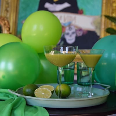 En bricka med två gröna drinkar och uppskuren limefrukt. I bakgrunden finns gröna ballonger.