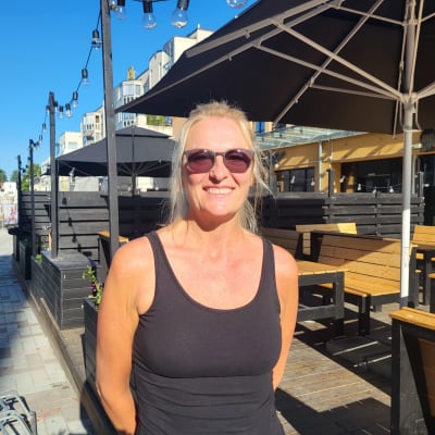 En kvinna i solglasögon står på en gågata.