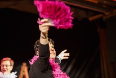 Kvinnlig skådespelare sträcker ut handen med en pink solfjäder.