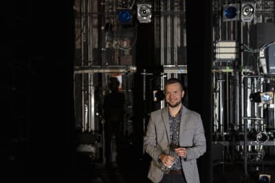 Demian Seesjärvi seisoo teatterin lavan tekniikkahuoneessa kädessään vesipullo.