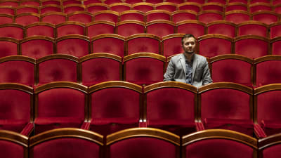 Demian Seesjärvi istuu teatterin katsomossa punaisten penkkien keskellä.