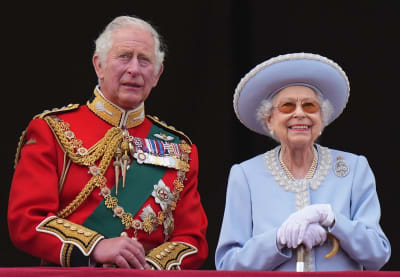 Prins Charles i röd uniformsjacka med många ordnar och drottning Elizabeth II i ljusblå hatt och dräkt.