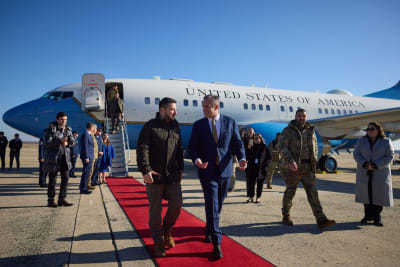 Volodymyr Zelenskyj på en röd matta framför sitt flygplan talandes med en man.