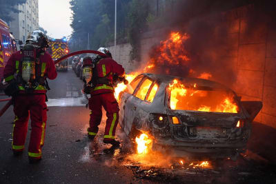 Kaksi palomiestä sammuttaa palavaa autoa.