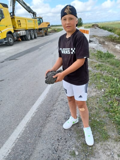En pojke visar upp en bit asfalt på en landsväg vid ett vägbygge