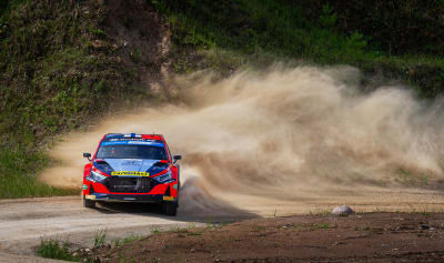 En rallybil kommer in i kurvan med sidan före. Farten är hög.