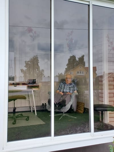En gammal man i rutig skjorta vilar i en vilostol på en inglasad veranda (Rune Björkqvist)