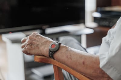 En äldre person med ett larm runt handleden, sitter framför en datorskärm.
