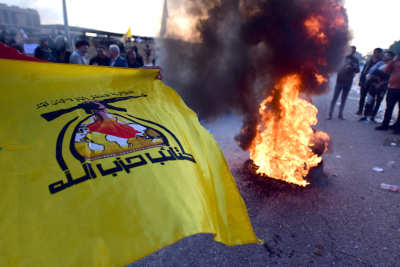 Milisgruppen Kataib Hizbollahs flagga i förgrunden på en arkivbild från 2020 i samband med en demontration utanför USA:s ambassad i Bagdad.