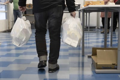 En man bär på två vita plastkassar med mat.
