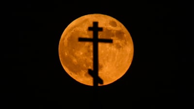 En blodröd måne syns bakom ett ortodoxt kors.