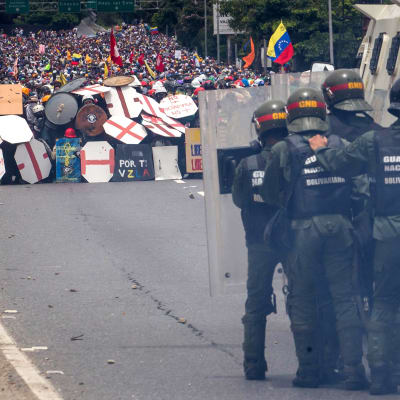 Polis med kravallsköldar och vattenkanoner står mittemot tusentals demonstranter som söker skydd bakom fanersköldar på en motorväg i Caracas.
