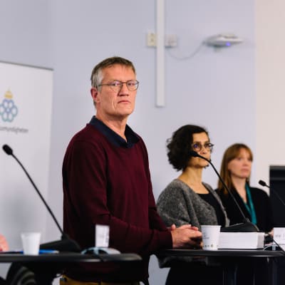 Anders Tegnell och andra personer står framför talarpodier och mikrofoner under en presskonferens.