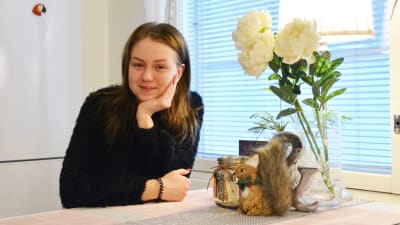 En ung kvinna sitter vid ett köksbord och lutar kinden mot den ena handen.