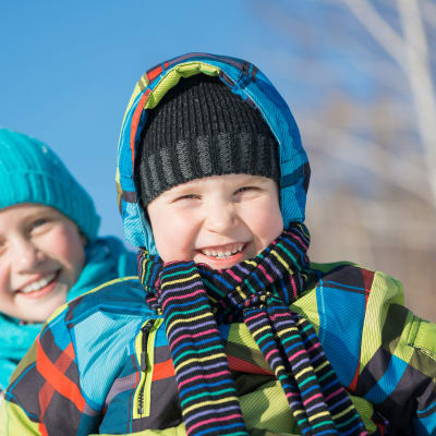 En pojke och en flicka i vinterkläder skrattar mot kameran