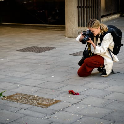 En fotograf tar en bild på Olof Palmes minnesplakett. Några blommor ligger invid plaketten.