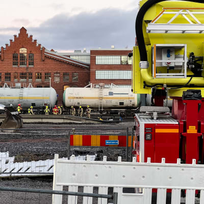 Personer från räddningsverket i gula och röda kläder undersöker en kemikalievagn på Åbo bangård.