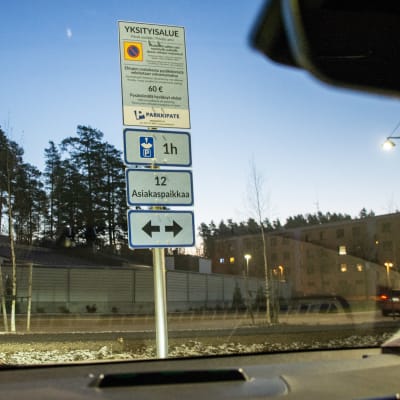 Skyltar med information om parkeringsövervakning står vid en parkeringsplats. Bilden är fotad från insidan av en bil.