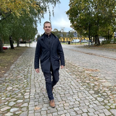 Tummavaatteinen mies kävelee kivisellä kadulla syksyllä.