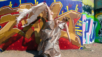 Marja Ahlsved och Heidi Kiviharju från Arosa Ensemble står iklädda klänningar framför en graffitimålning..