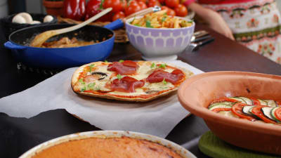 En köksbänk med flera tomaträtter uppdukade, så som tomatpaj, ratatouille, pizza, korv stroganoff och tomatpasta.