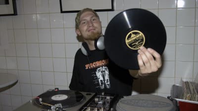 Rapartisten Paleface visar upp en LP, sitter bakom ett DJ-bord.