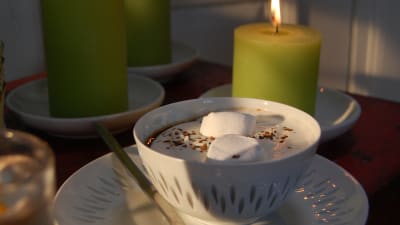 En kopp med varm choklad toppad med marshmallows, vispgrädde och lite kaffepulver.