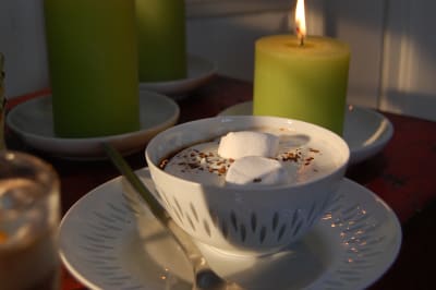 En kopp med varm choklad toppad med marshmallows, vispgrädde och lite kaffepulver.