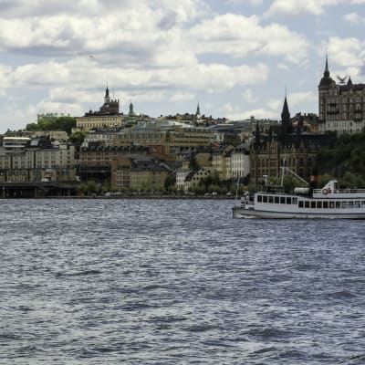 Vy över stadsdelen Södermalm i Stockholm, med Riddarfjärden och en båt i förgrunden.