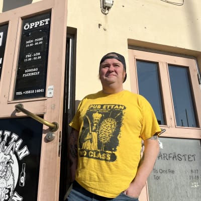 En man i gul t-tröja står vid en dörr till en pub.