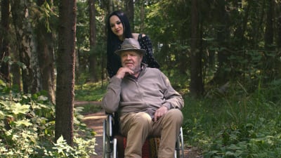 Lenita Susi skjutsar Vesa-Matti Loiri i rullstol genom skogen