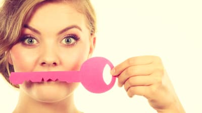 Kvinna ser in i kameran, håller upp stor rosa leksaksnyckel framför munnen