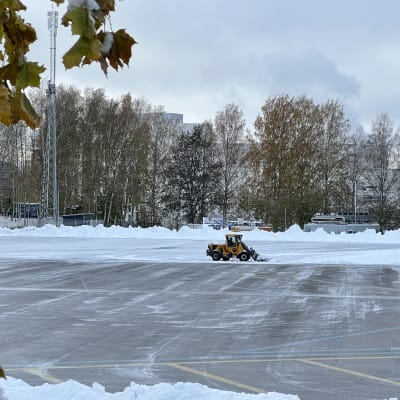 Tampereen Kalevan liikuntapuiston, Sorsapuiston, tekojäätä ollaan tekemässä. Kuvassa aura-auto raivaa pois lumia kentältä, ympärillä suuria lumikinoksia. Kuvauspäivä 2.11.2023.