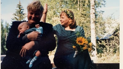 Valokuva-albumiin sivu, jossa kaksi kuvaa traktorin peräkärrystä, toinen takaa, toinen edestä. Kärryssä istuvat Iiro Rantala, Lotta Kuusisto ja heidän Topi-vauvansa. 