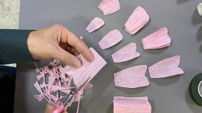 kädet leikkaa kreppipaperista kukanlehtiä
