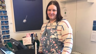 ung kivinna i vit tröja med röda och blåa ränder och ljusblått förklade med muminfigurer . Står vid kassaparat