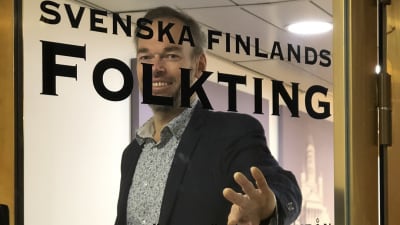 Markus Österlund öppnar glasdörr med texten Svenska Finlands Folkting.