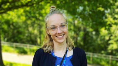 Nicole Mattsson i klädd glasögon ler fram för en väg omgiven av träd.