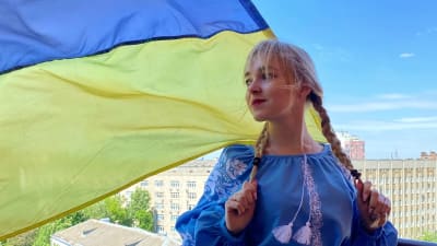 Ung blond kvinna med flätor med Ukrainas flagga bakom sig